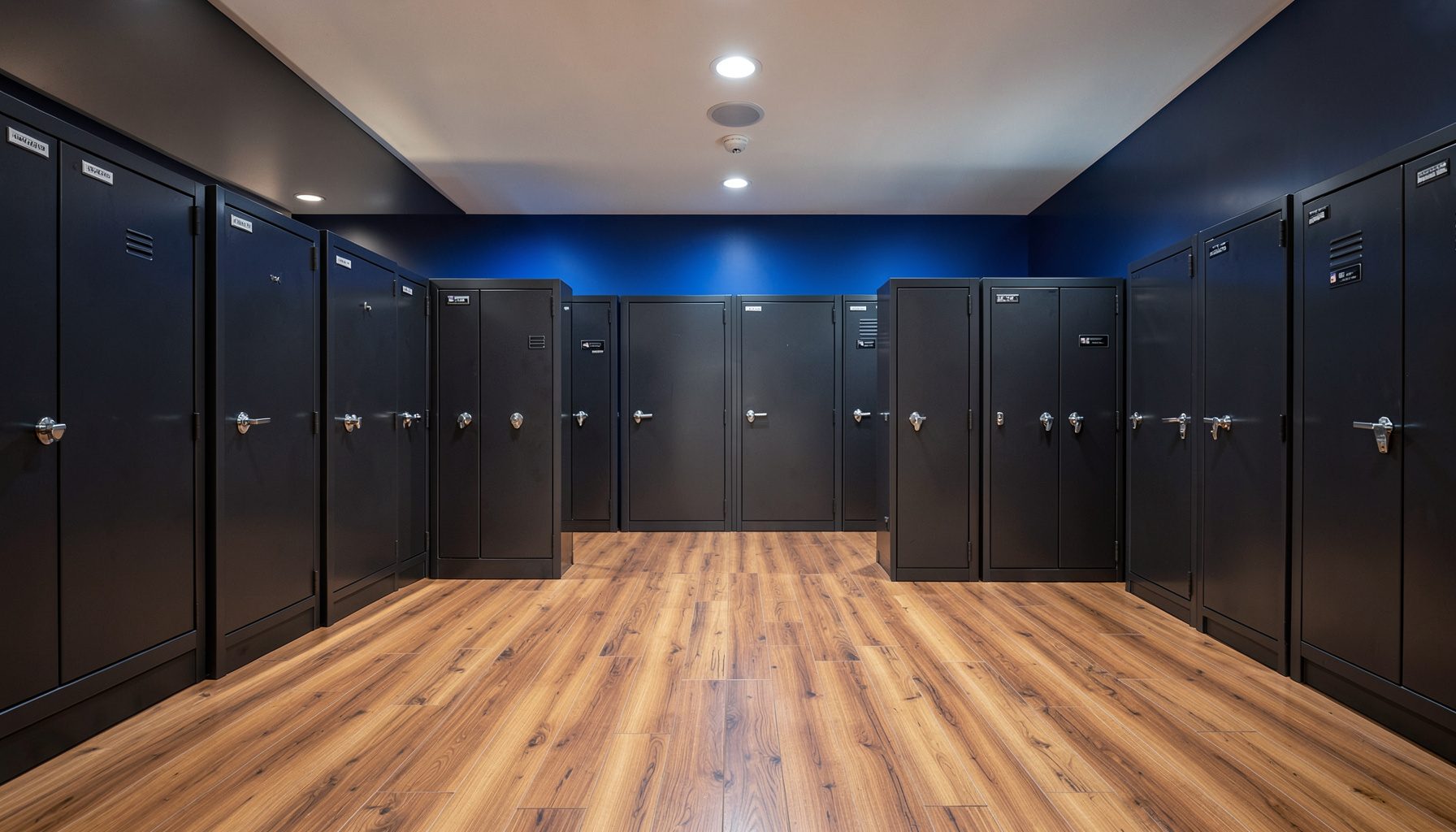 A clean architectural photograph with strong symmetry showing a row of sturdy gun safes in a well-lit showroom, deep charcoal and steel tones against warm wood flooring